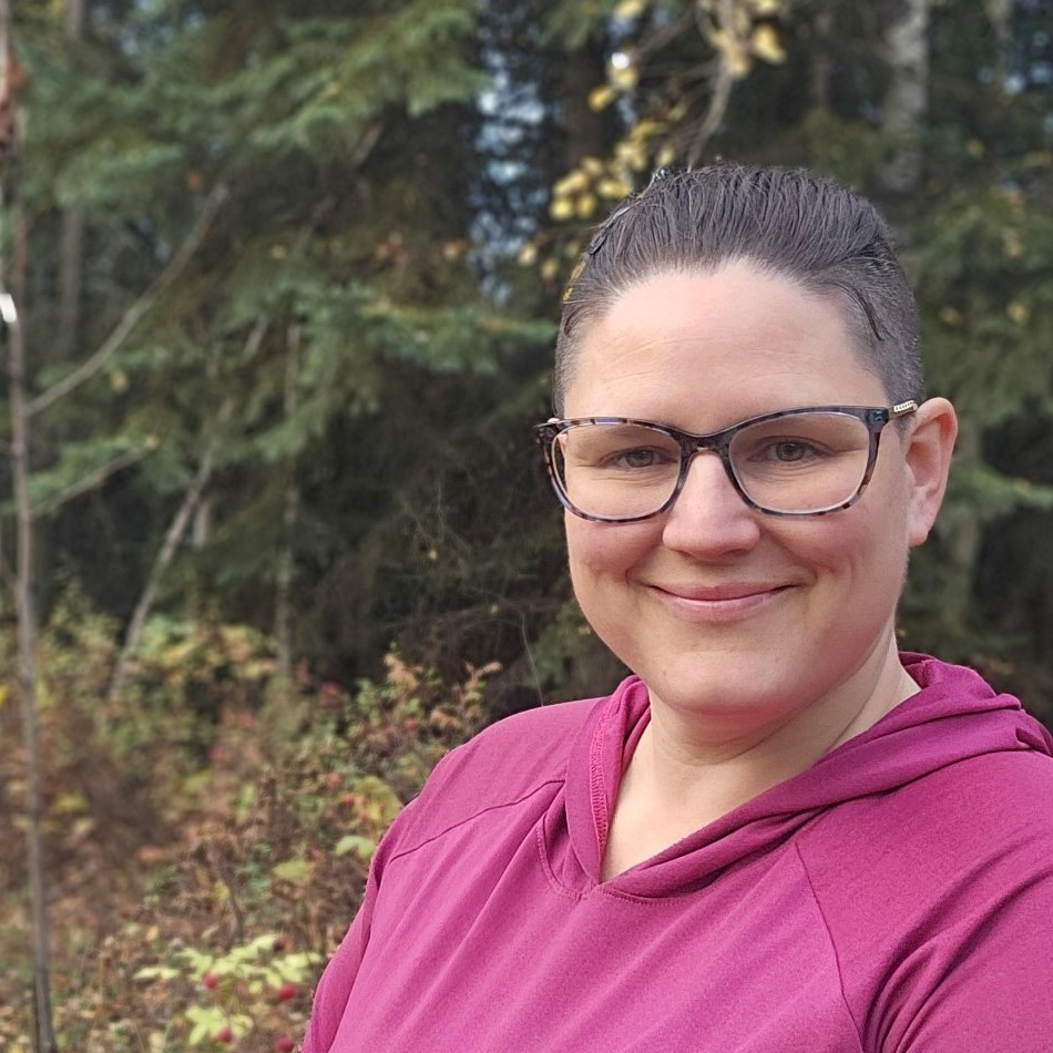 Ashley Glover in a magenta hoodie in the autumn woods, smiling and looking directly at the camera.